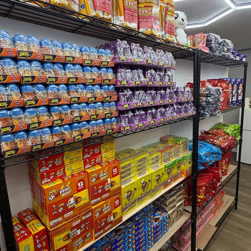 Shelves display brightly packaged Latin American snacks, crackers, cookies, and candy in a brightly lit store aisle.
